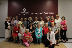 A group picture of the women that graduated in 1974 in front of the School of Nursing sign